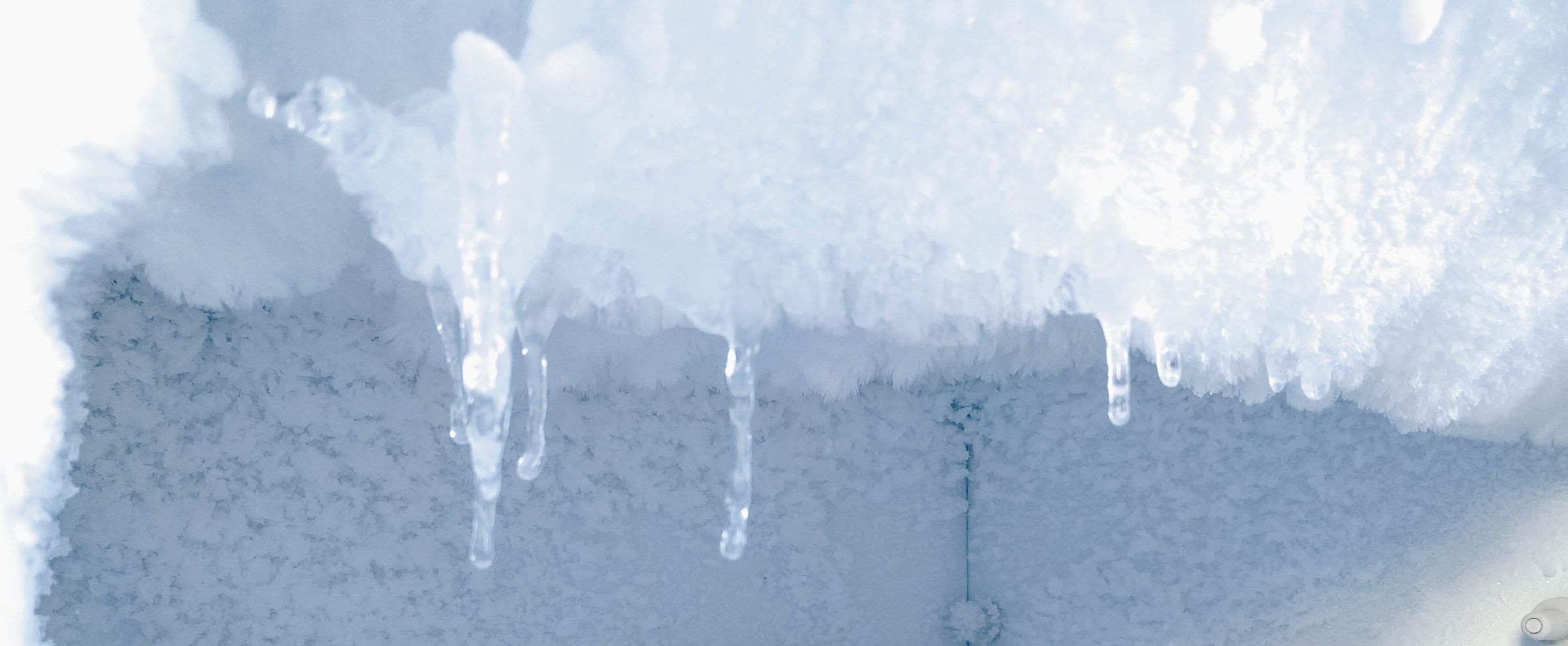Thick frost and icicles hanging from the top of a freezer compartment