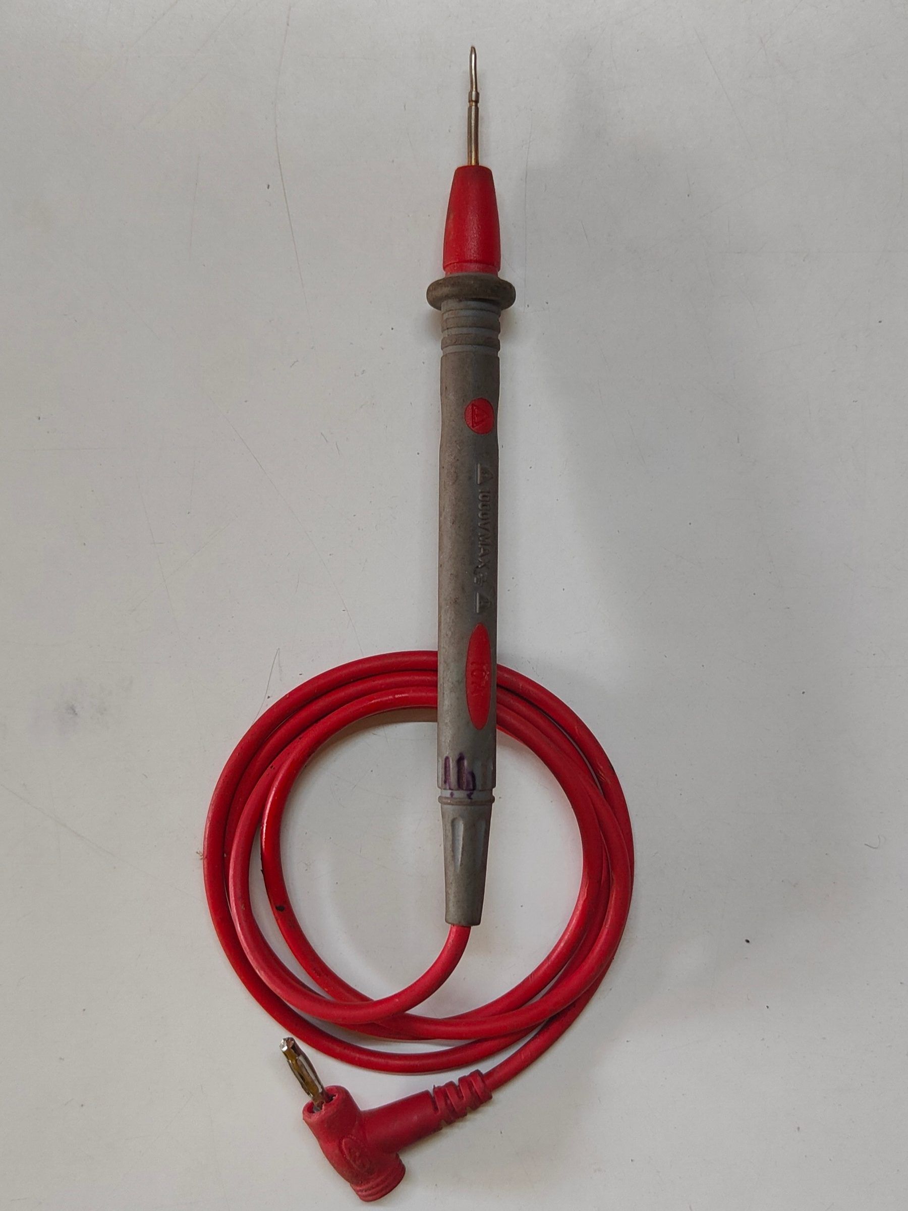 Punta de prueba de un multímetro con la punta roja y un cable rojo enrollado sobre una superficie gris clara