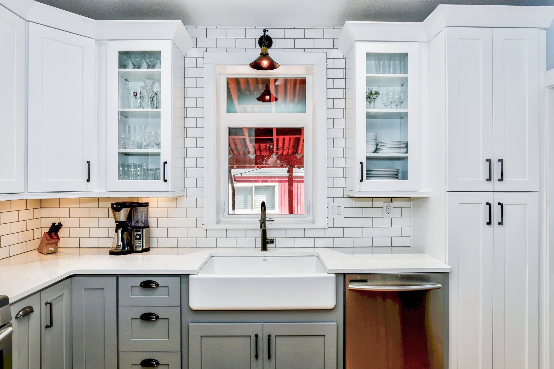 White shaker kitchen with a farmhouse sink under a window, subway tile and a stainless dishwasher